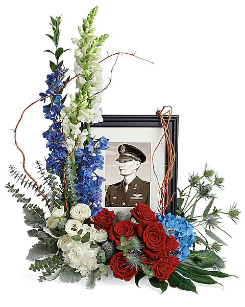 Floral arrangement with red, white, and blue flowers around a framed portrait of a military officer.