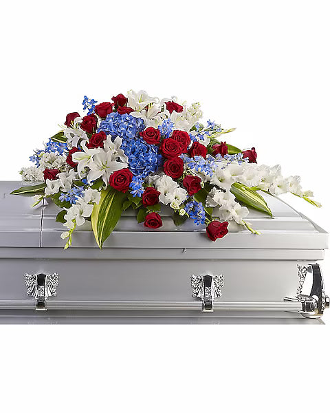 Casket with a floral arrangement of red, white, and blue flowers on a white background